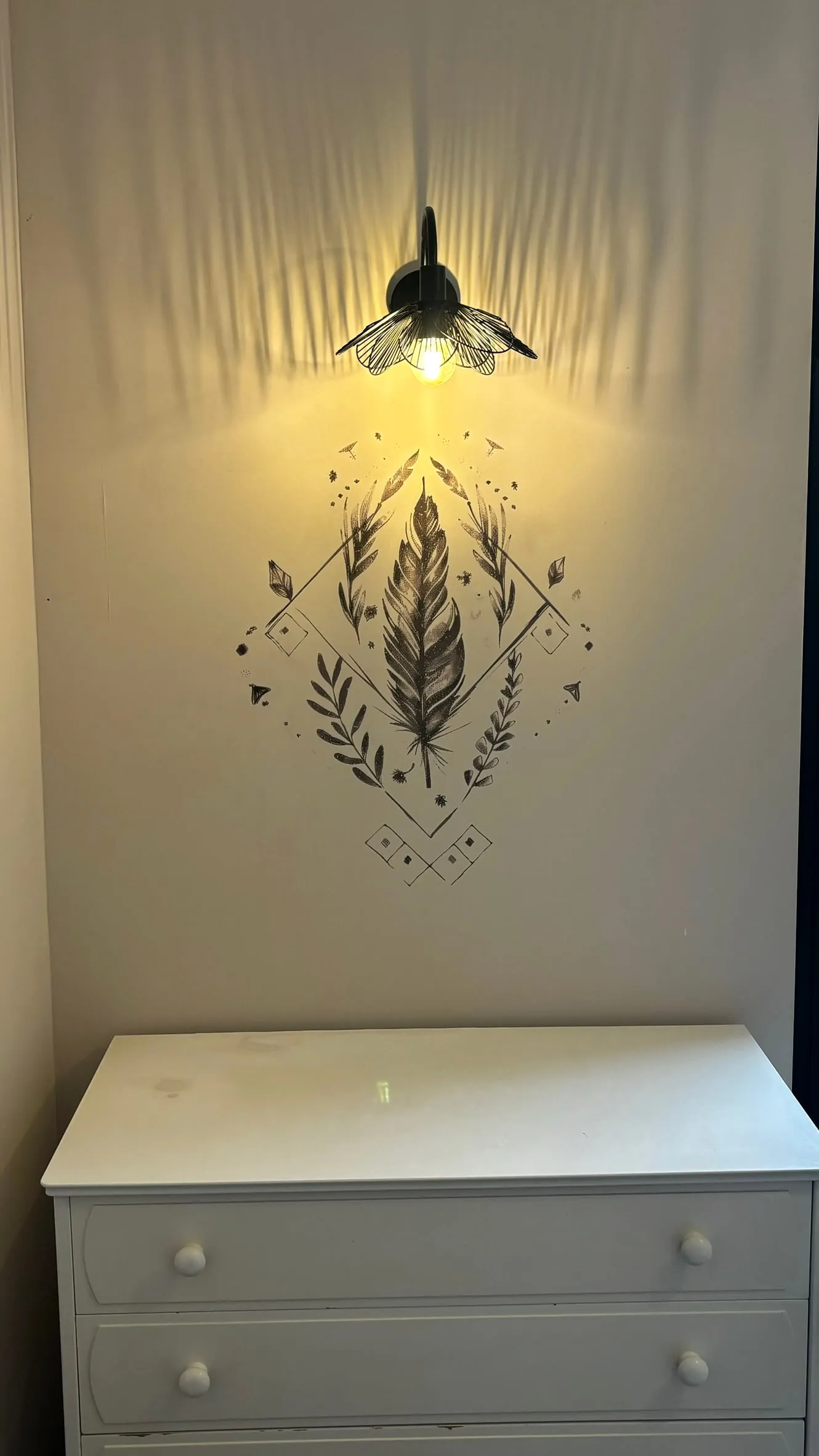 Chambre : un motif de plume à l'encre imprimé sur le mur, sous une applique allumée